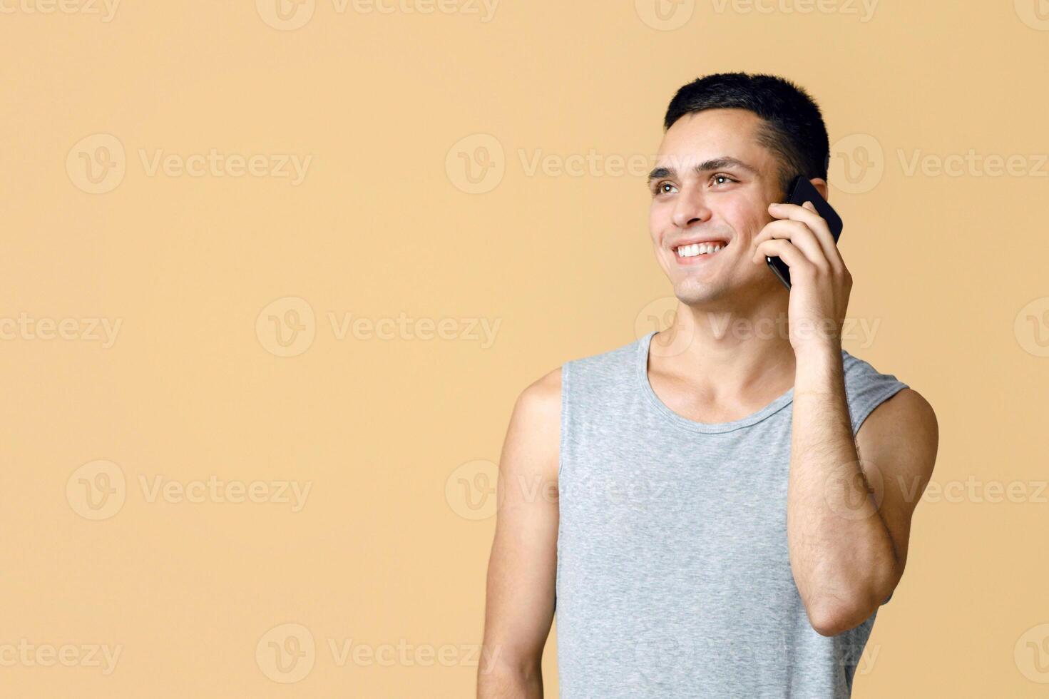 Modern communication and important call during self-isolation at home. Cheerful handsome man student in casual speaks on phone and looks at empty space, isolated on light background, studio shot photo