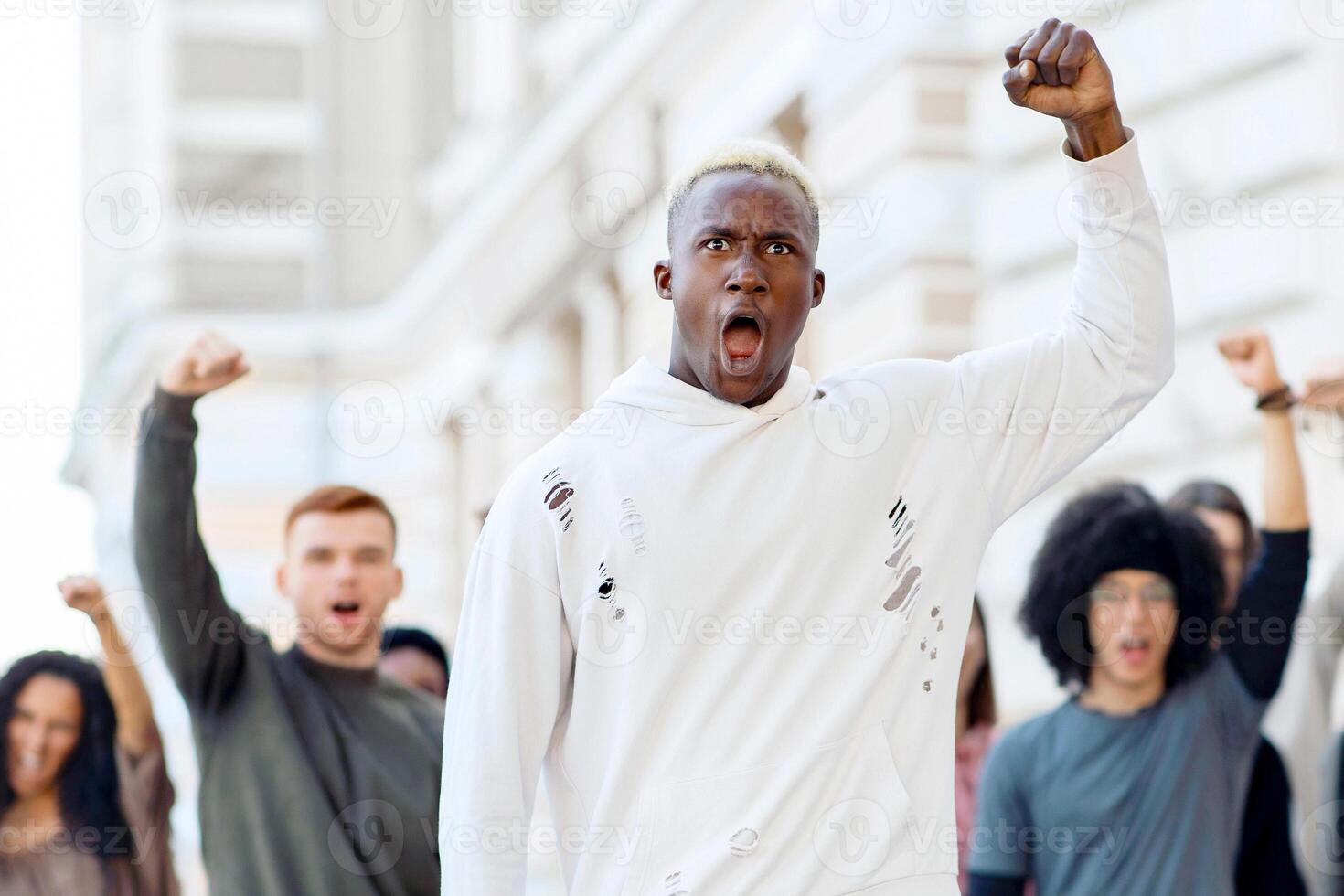 Black man raising fist up and yelling, leading international group of students. African american man leader standing in front of multiracial group of protestors on the street, copy space photo