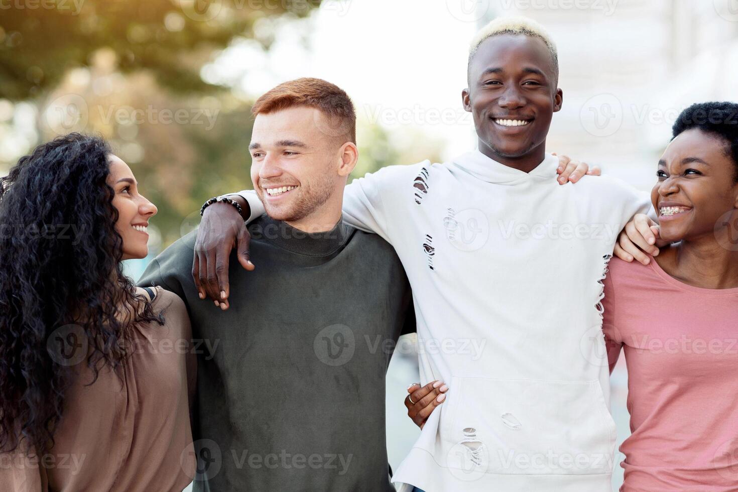 International group of friends in casual outfits smiling and hugging on the street, carefree multiracial students standing in a row and embracing outdoors, having conversation, closeup, panorama photo