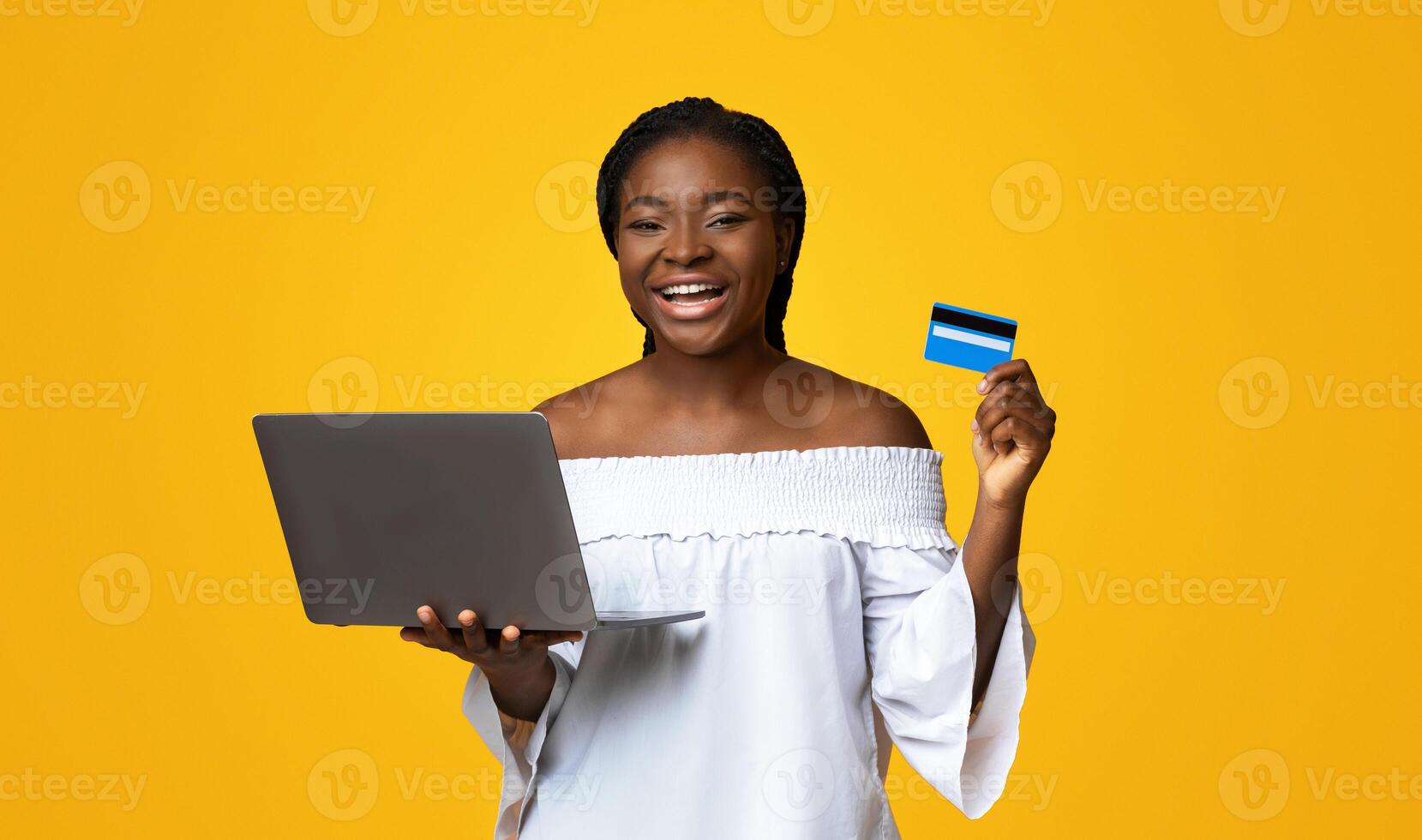 Online Payment. Cheerful black lady with laptop and credit card posing on yellow background, making shopping in internet, transferring money, booking vacation or paying utilities, copy space photo