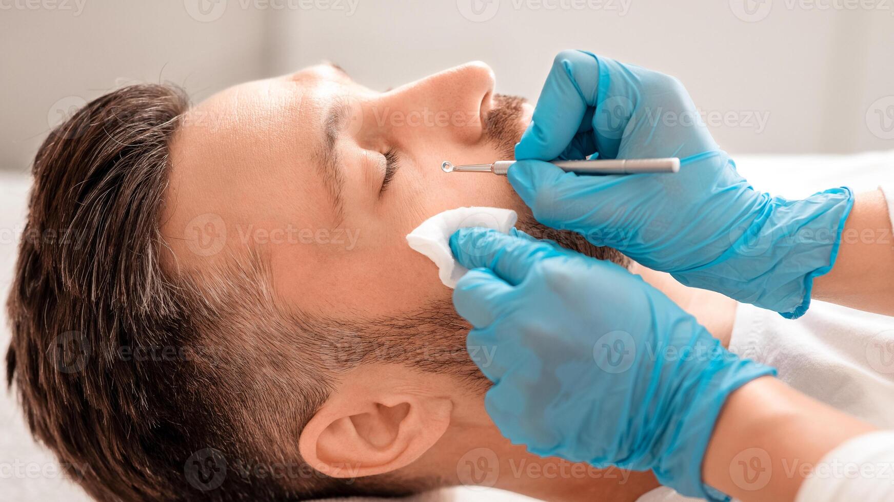 Male cosmetology concept. Unrecognizable cosmetician using blackhead remover for cleaning middle aged man face in spa salon, closeup. Spa attendant in medical gloves cleaning man skin photo