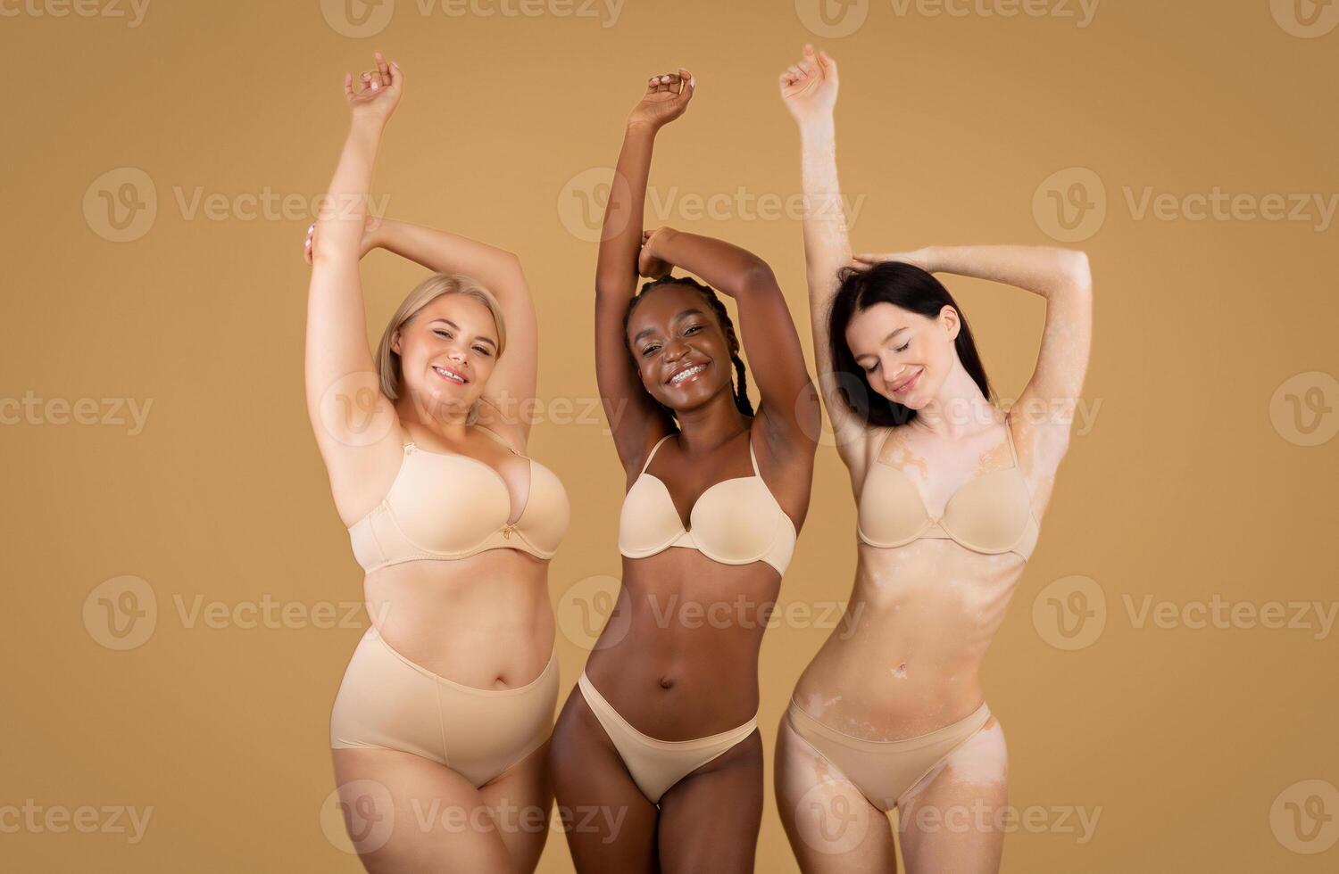 Love Your Body. Happy Three Women With Different Shapes And Appearance Posing Over Beige Studio Background, Positive Beautiful Multi-Ethnic Ladies In Underwear Enjoying Themselves, Copy Space photo