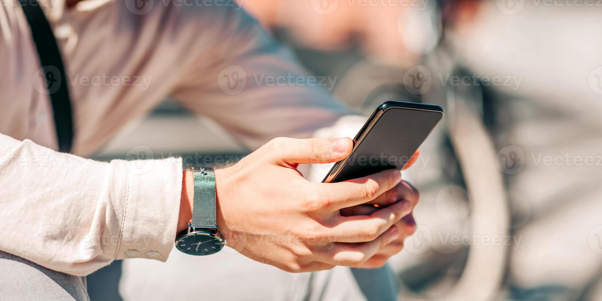 Online in city. Smiling attractive guy in shirt sits on street and looks at smartphone, close up, cropped, free space photo