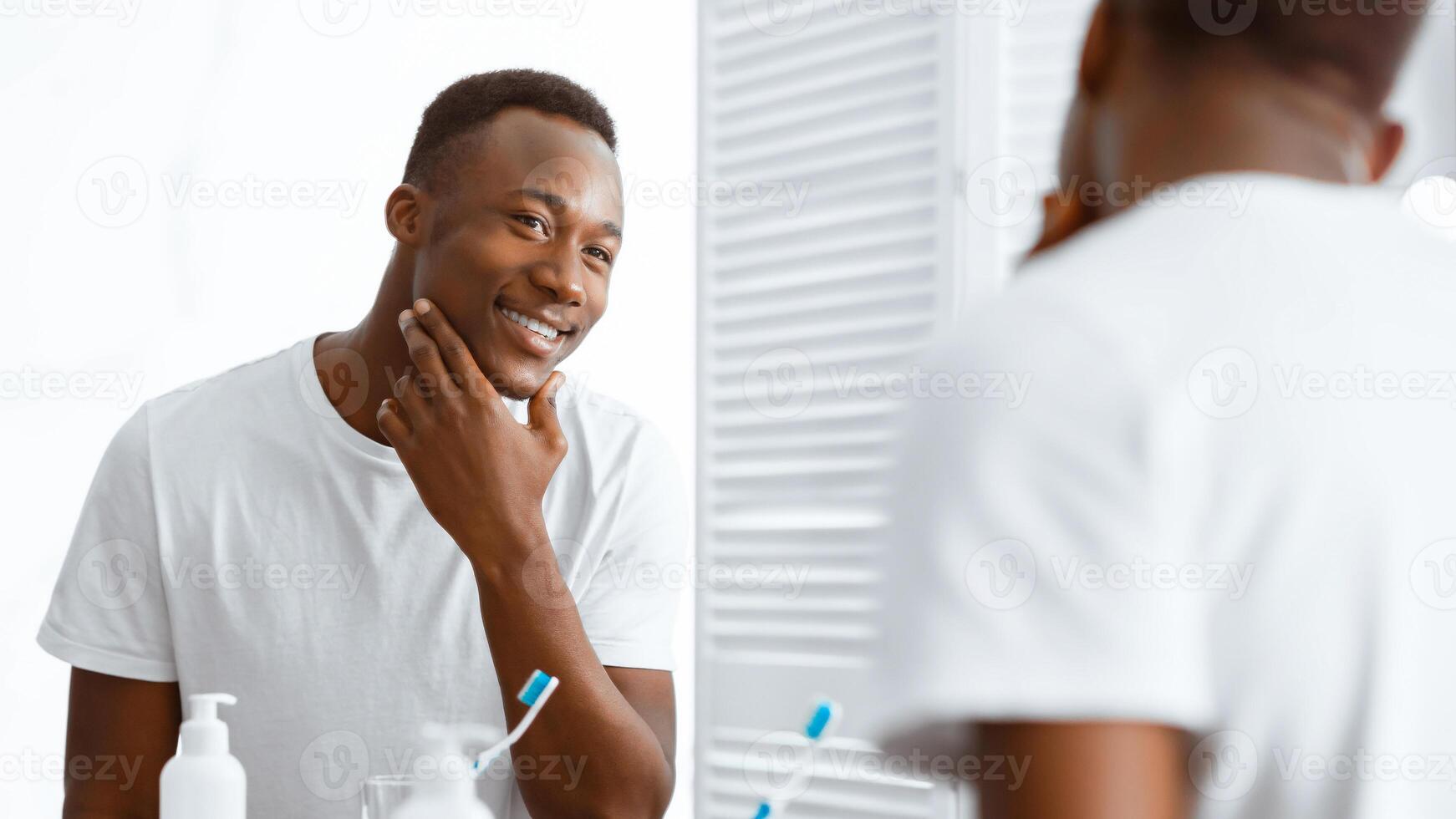 Well-Shaved African American Man Touching Smooth Face After Shaving Standing In Bathroom Near Mirror At Home. Male Beauty, Morning Self-Care Routine And Facial Skincare Concept. Panorama photo