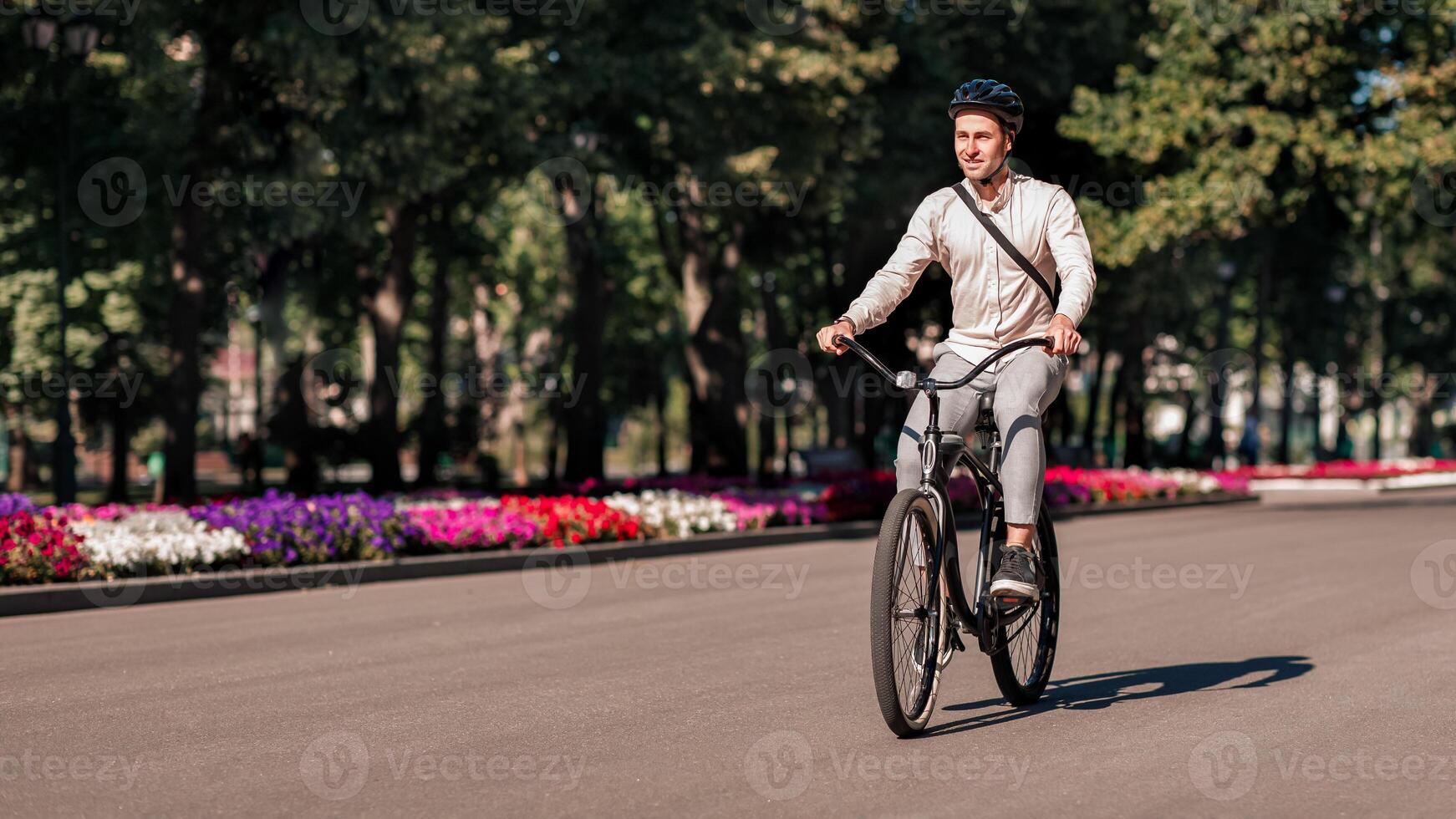 Urban eco transport, way to work and great walk in city park. Millennial man employee manager in safety helmet and casual, rides on bicycle outside in summer and enjoys nature, outdoor, free space photo