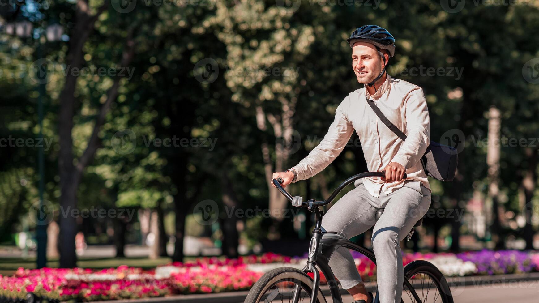 Businessman in park and active sports lifestyle in city. Smiling millennial employee in protective helmet rides on bike to work at summer and enjoys nature, outdoor, side view, free space photo