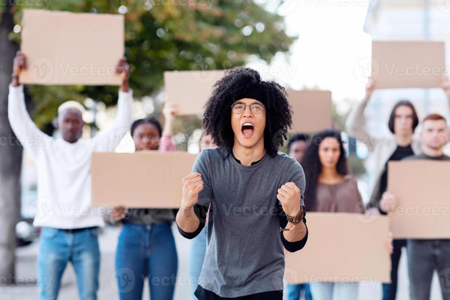 Emotional mixed race guy leading a group of demonstrators on the street. International diverse group of people with blank placards protesting for human or animal rights and against racism photo