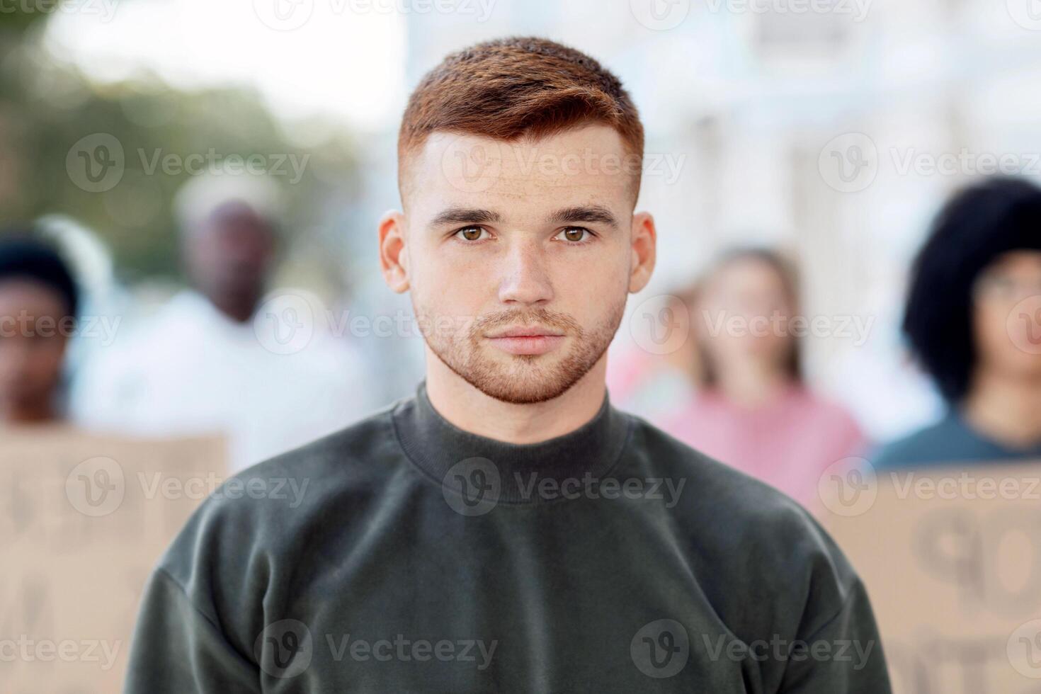 Strike, riot, protest, demonstration concept. Serious young guy standing over crowd with placards, male leader leading multiracial group of strikers chanting slogans, selective focus on man photo