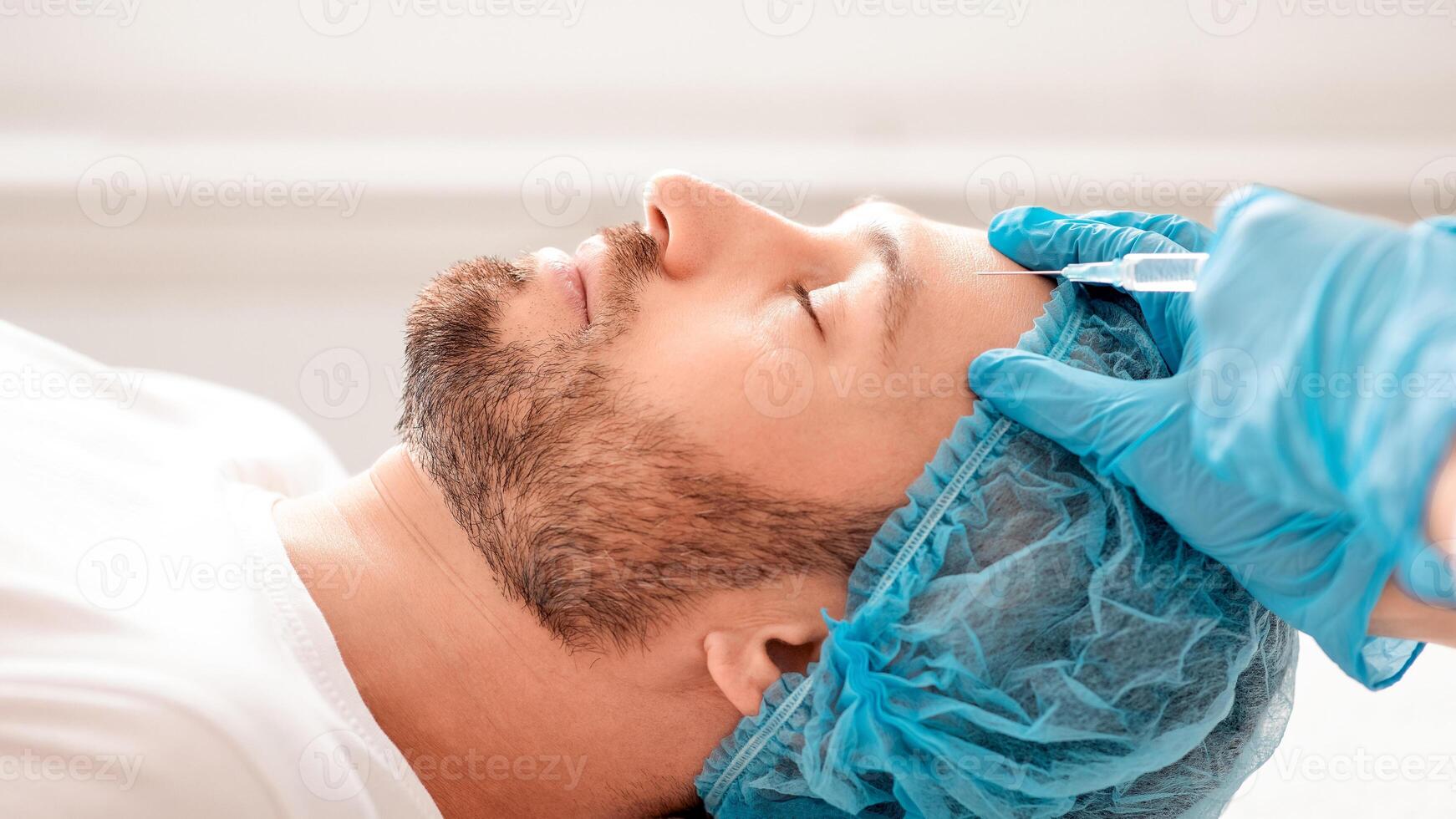 Closeup of bearded businessman in hairnet getting anti-aging filler at aesthetic clinic, side view. Plastic surgeon in protective blue gloves injecting hyaluronic acid in middle-aged man forehead photo