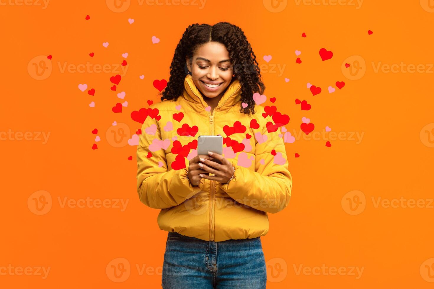 Happy African Woman Using Phone Sending Hearts And Like Icons Texting On Valentine's Holiday In Online Dating App Standing Over Yellow Studio Background. Love Chat, Romance And Networking photo