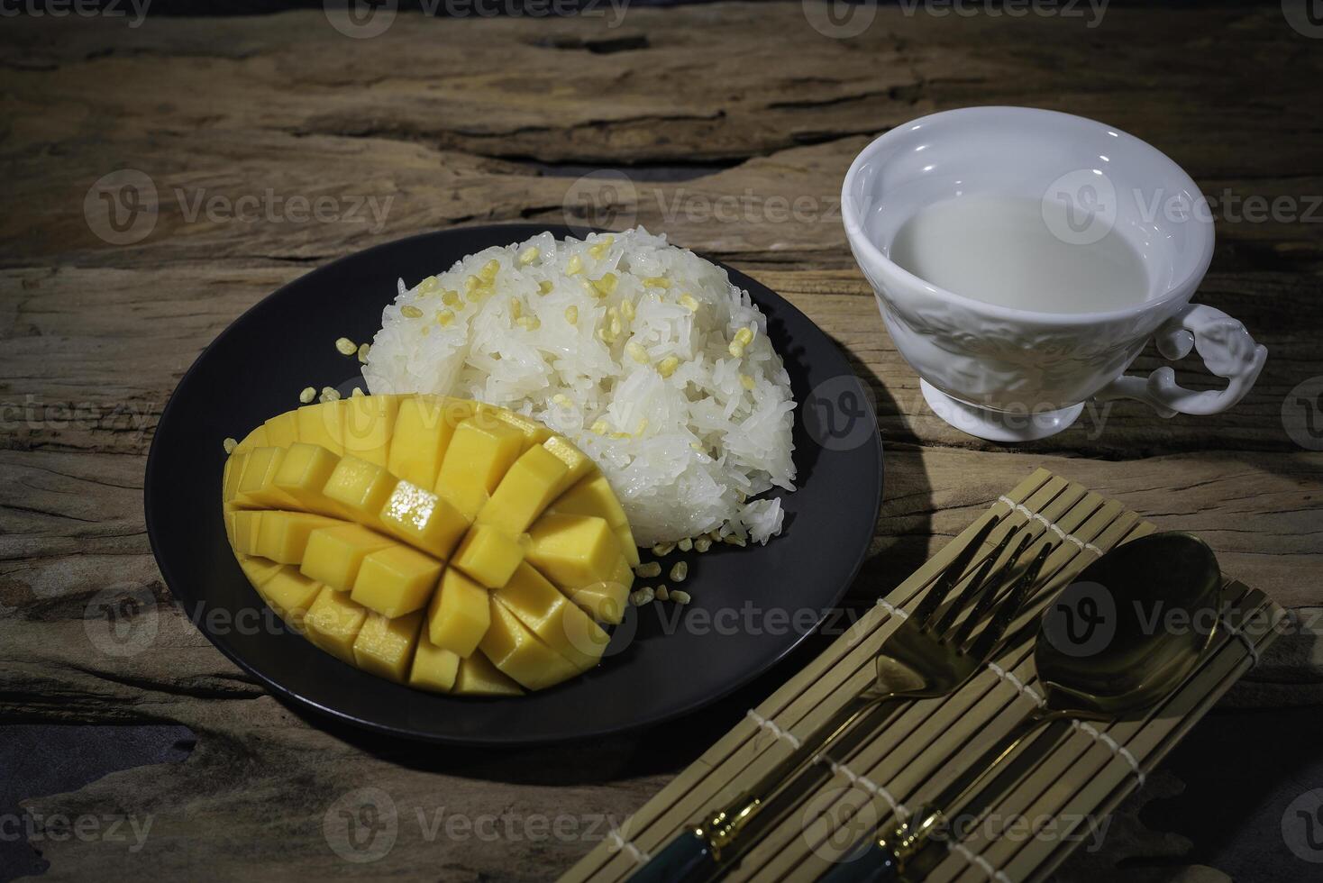 Mango sticky rice, a Thai food, with an old wooden backdrop. This food is very popular in most Asian countries. In Thailand, there is coconut milk in a white cup. photo