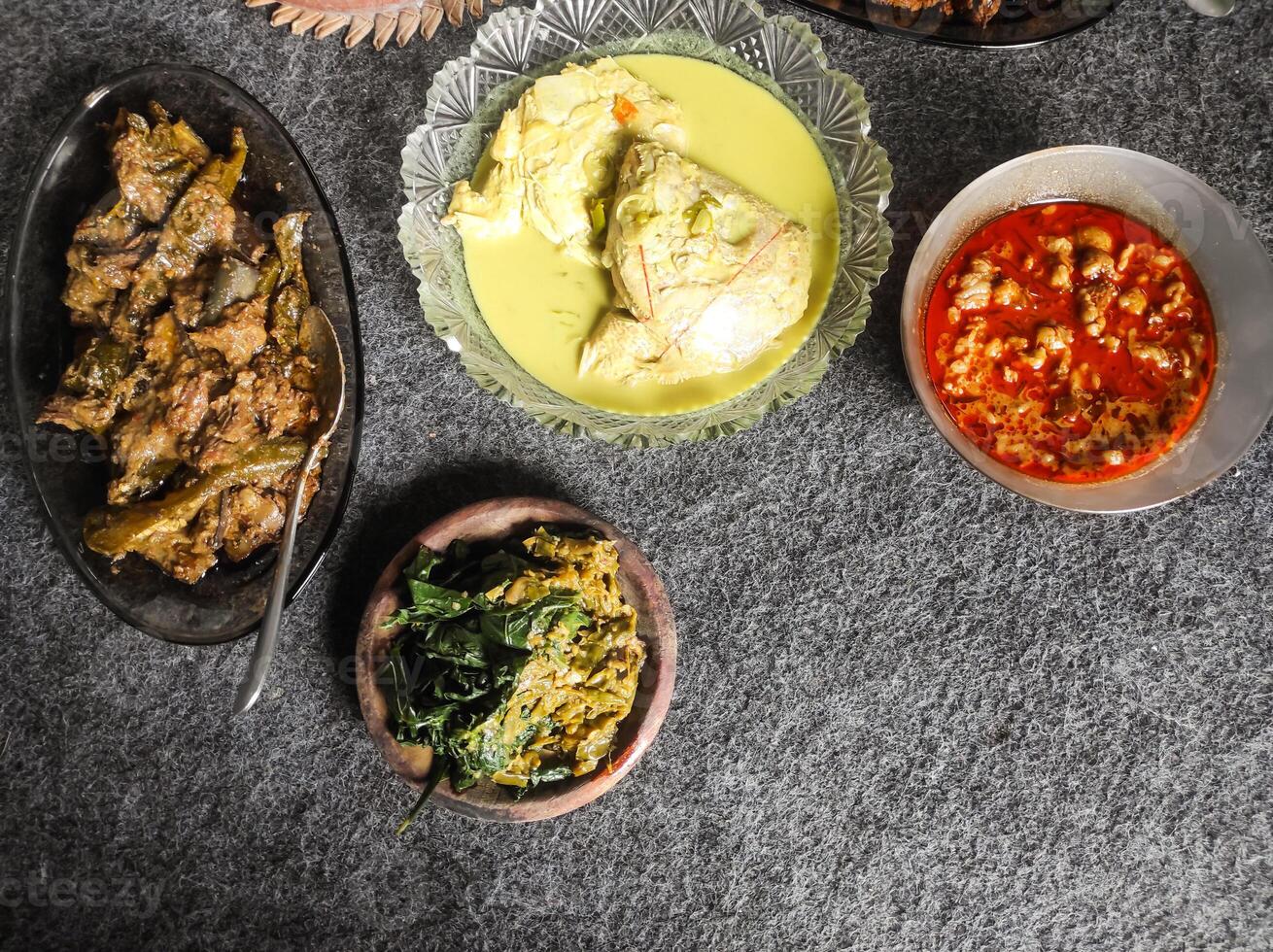 Photo of Padang cuisine served on a plate. The dish consists of snapper head curry, fried shrimp satay, red chili sauce, cassava vegetables and grilled eggplant. Tasty Indonesian gourmet.