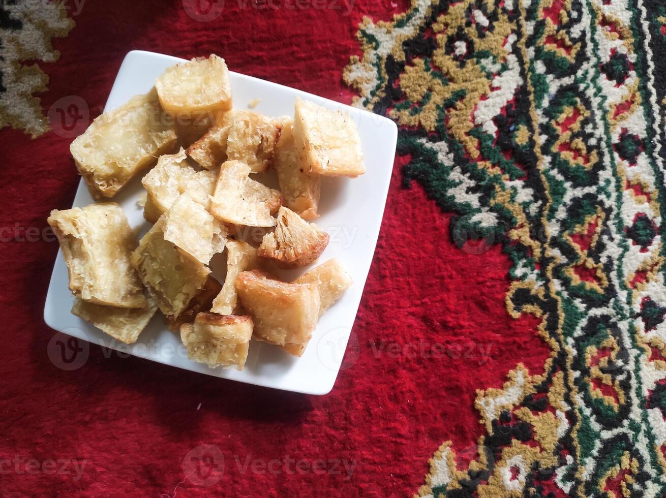 Photo of a plate of fried cassava. Fried food served on a white plate on a red Persian carpet. Traditional Indonesian cuisine. Soft and crunchy texture. Tasty Gourmet. Food Photography closeup