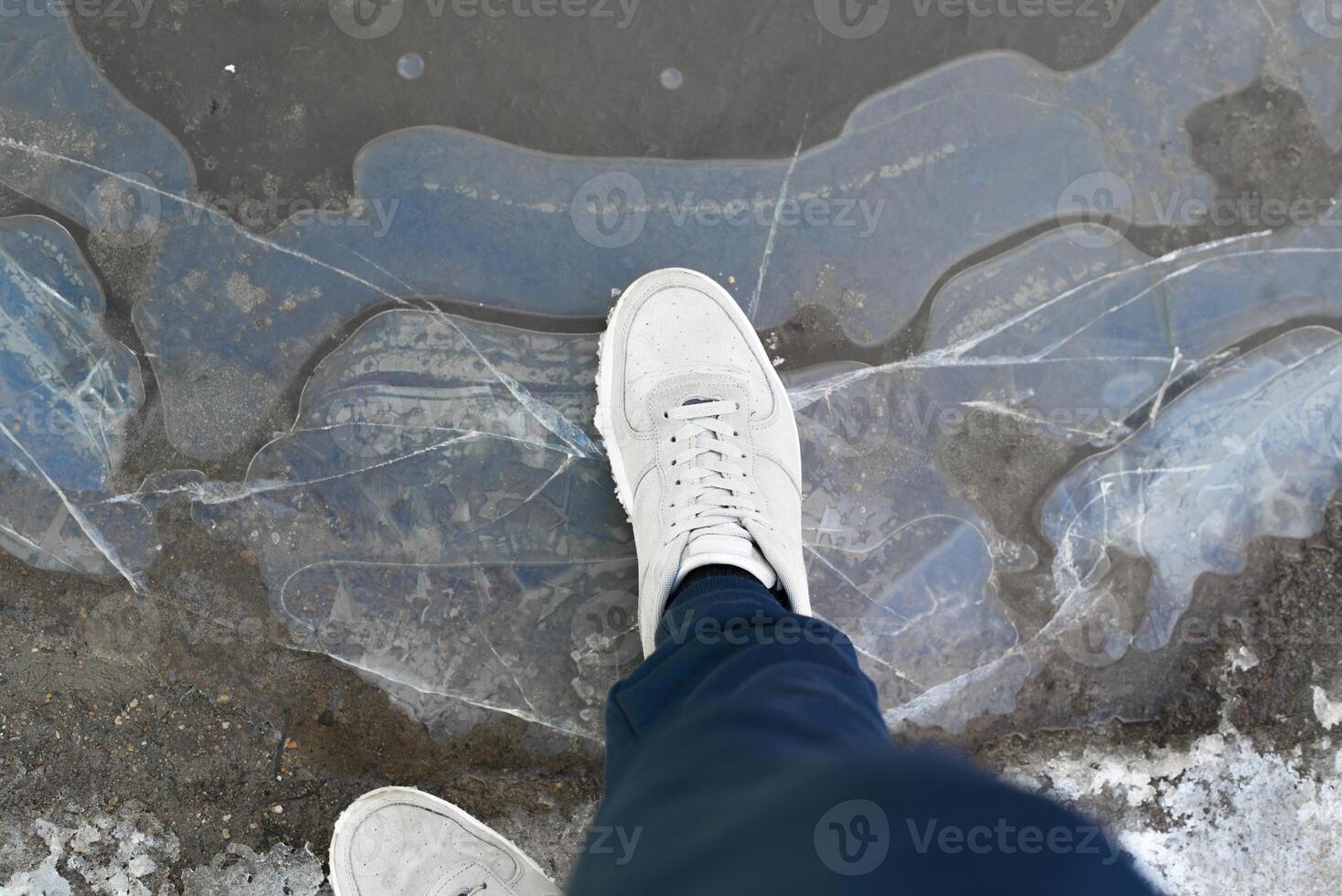 Man stands on cracked ice, top view. Men's boots on ice surface outdoors, pov photo