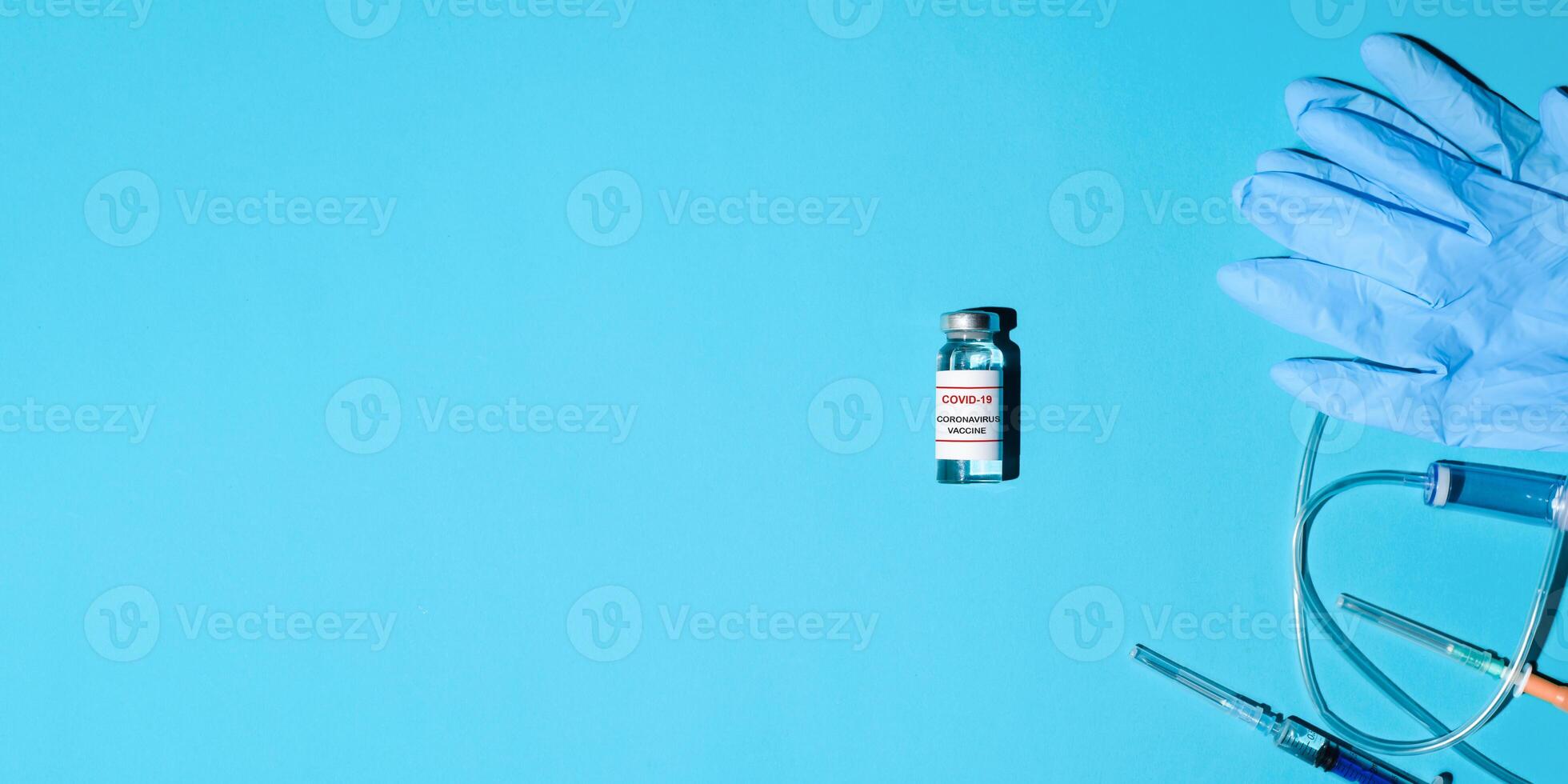Vial of anti-covid vaccine, syringe with medicine and medical gloves on a blue background, flat lay. Banner with medical advice for vaccination, copy space. photo