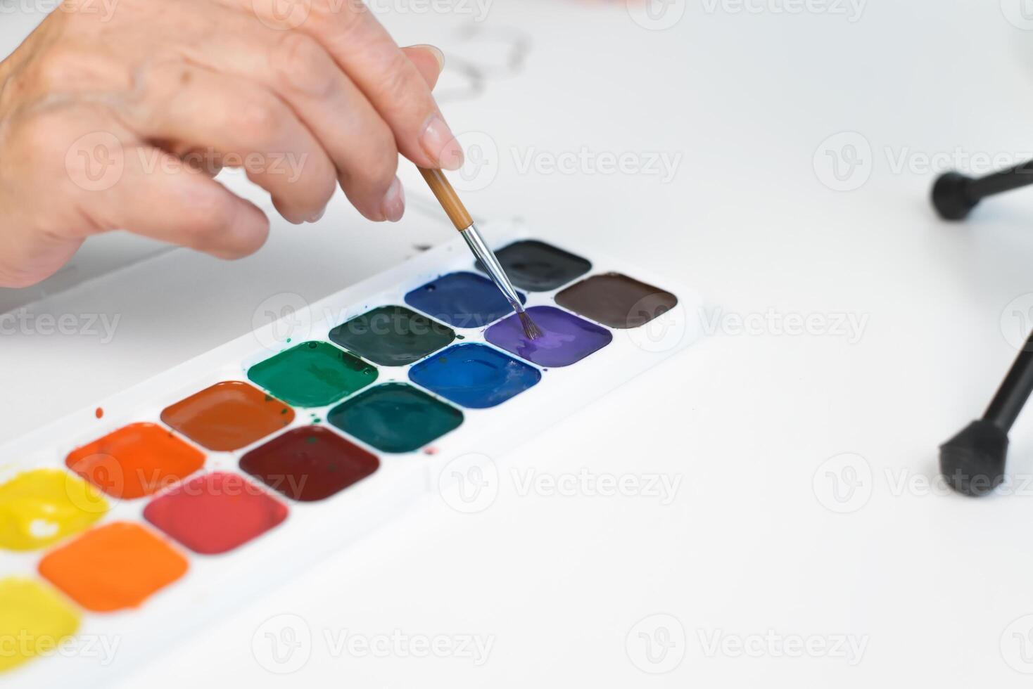 A person is holding a paintbrush and painting with watercolors photo