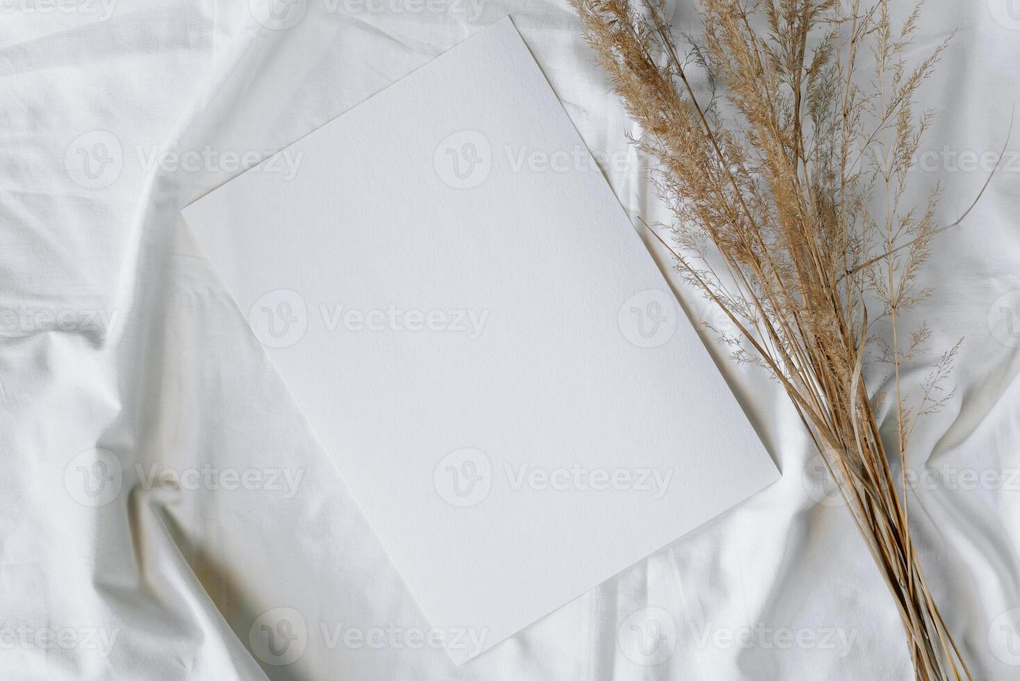 Blank sheet of textured paper and bouquet of dry herbs lying on a white fabric, flat lay. Mockup with copy space photo