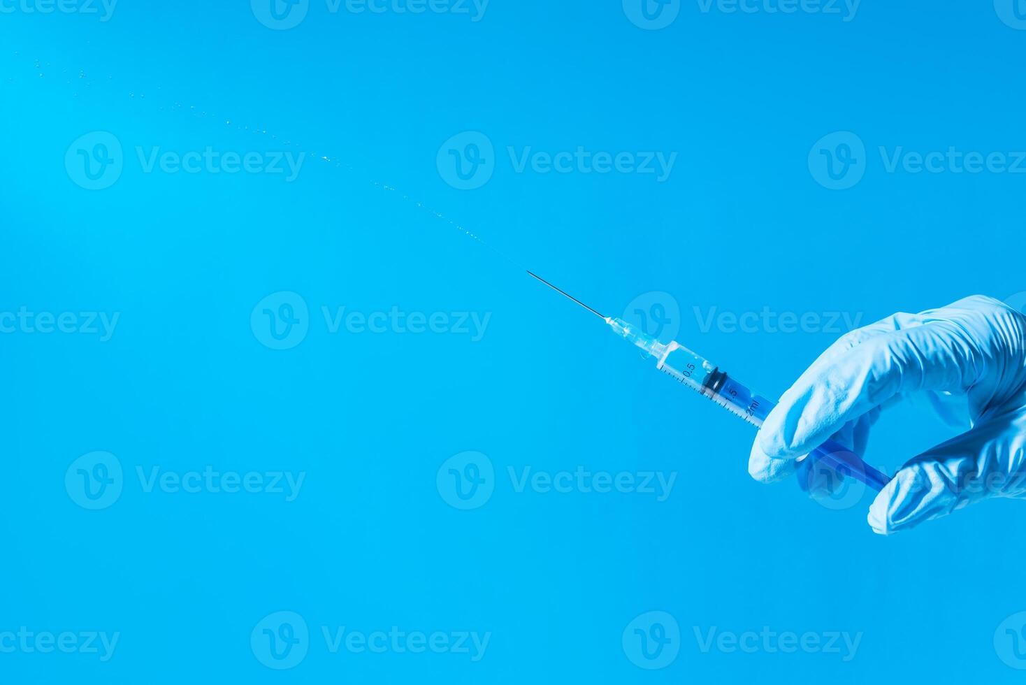 Hand in medical glove holding syringe with medicine, copy space. Injection with syringe on a blue background. Vaccination concept. photo