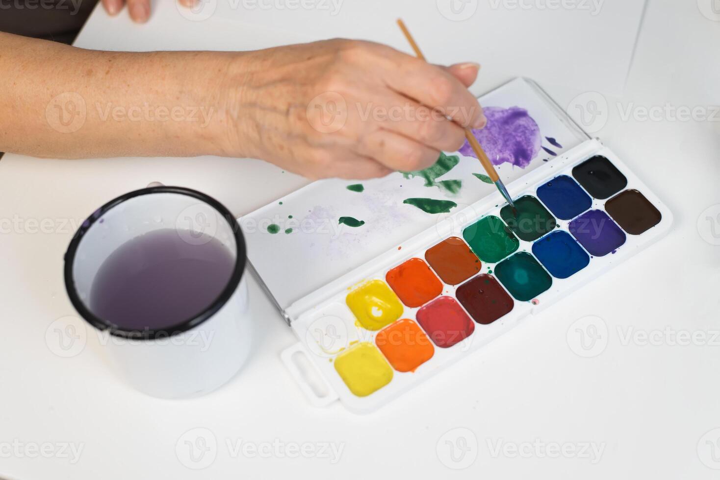A woman's hands are holding a paintbrush and a cup of water photo