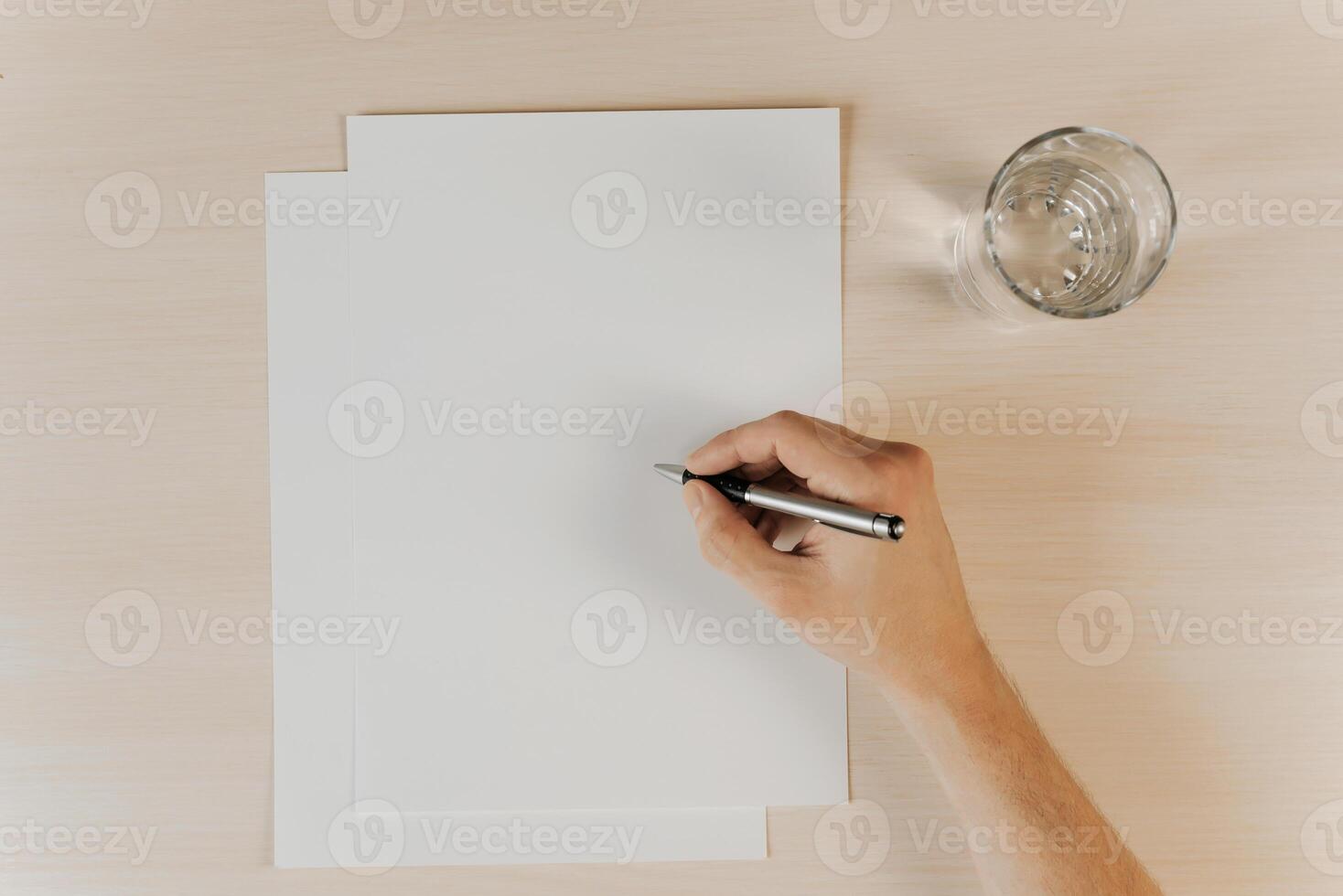 Blank paper, glass of water and hand holding pen, top view. Flatlay, mock up. photo