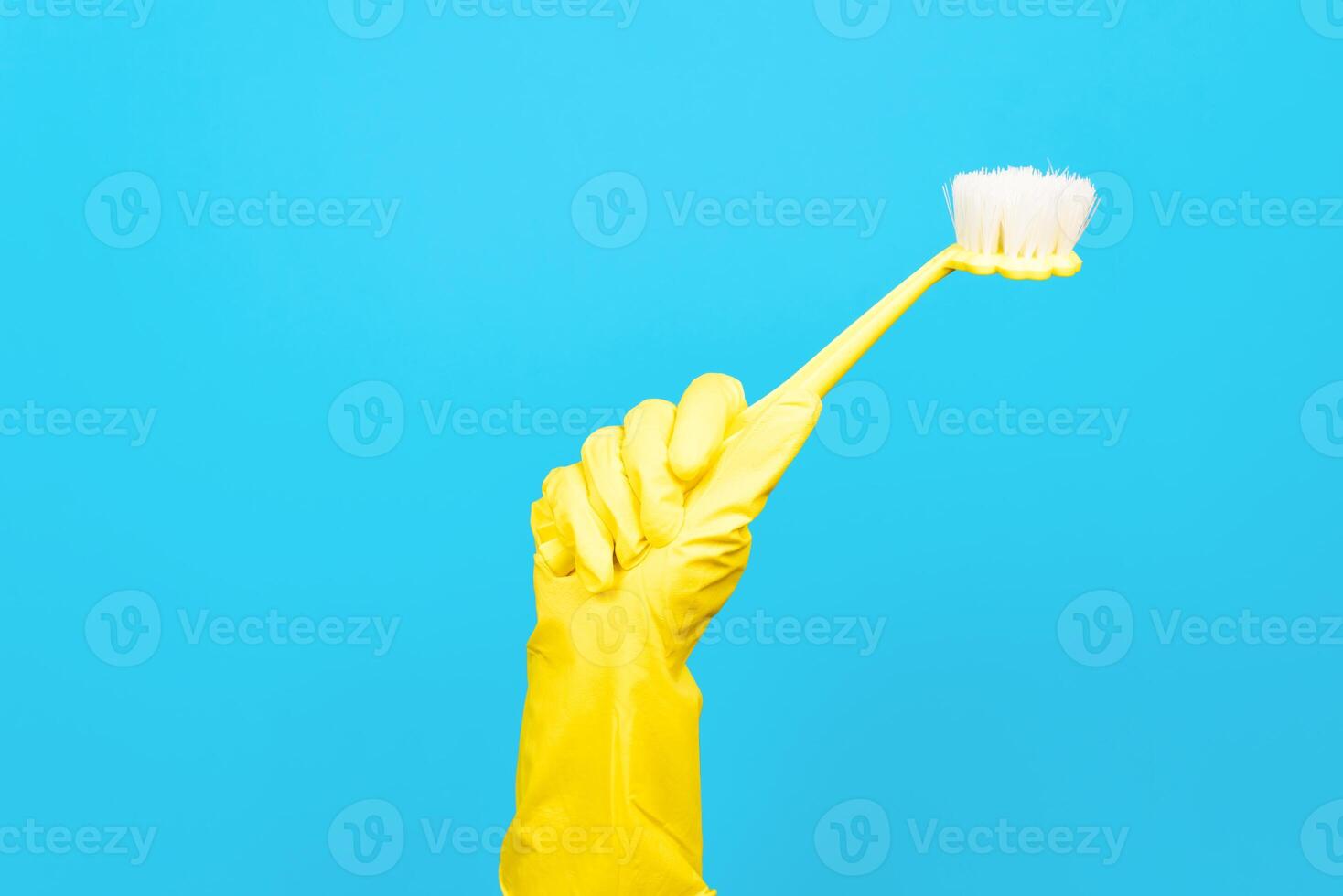Hand in yellow rubber glove holding brush for cleaning on blue background. Household cleaning equipment concept photo