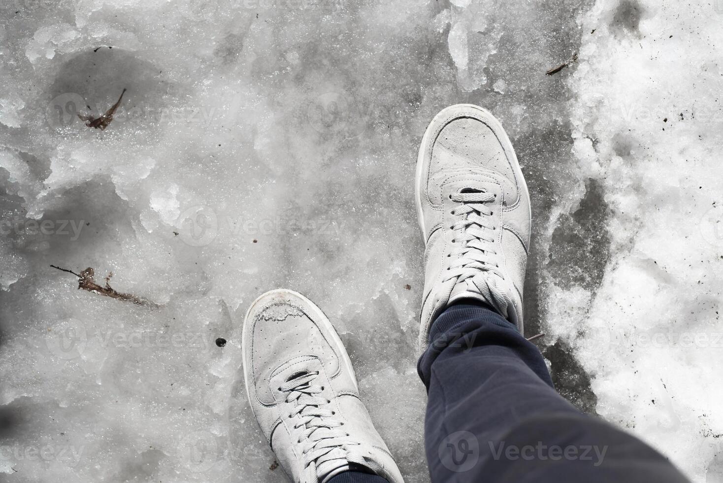 Legs in sneakers standing in the melting snow on the sidewalk. First-person view. Spring thaw concept photo