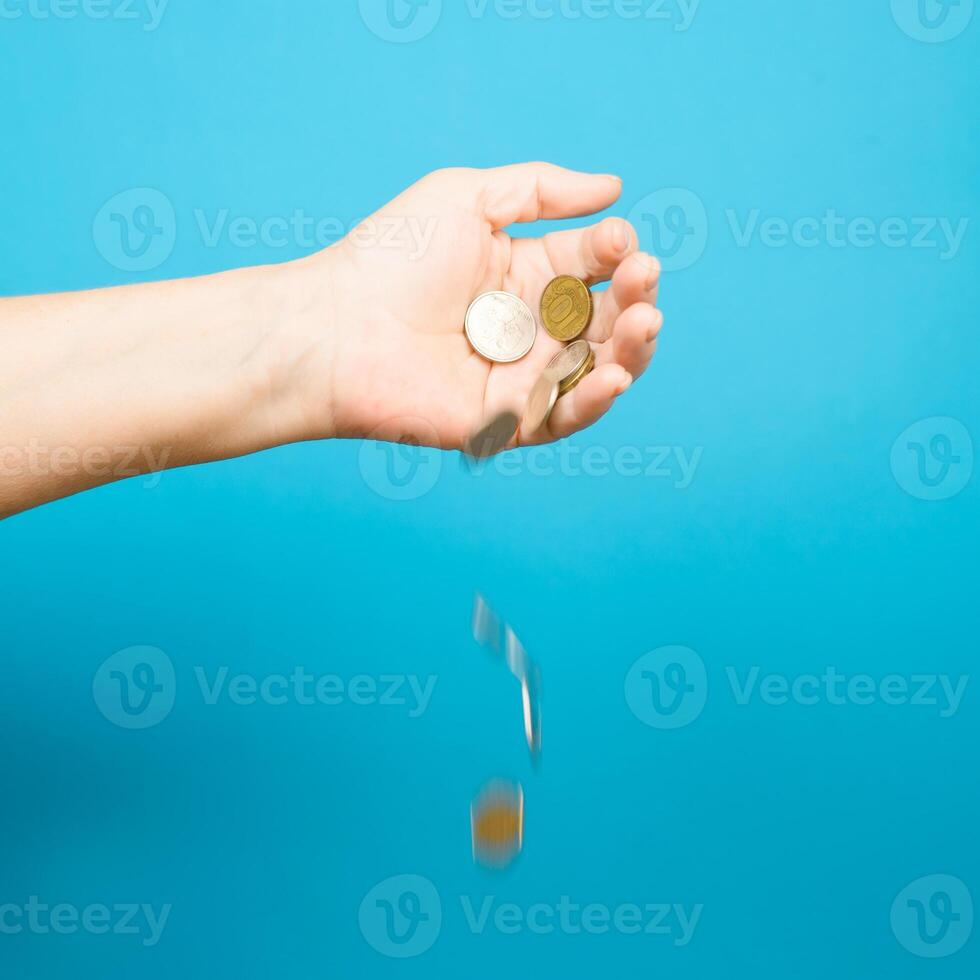 Elderly woman's hand and falling coins, blue background. Selective focus, motion blur. Income loss, poverty concept photo