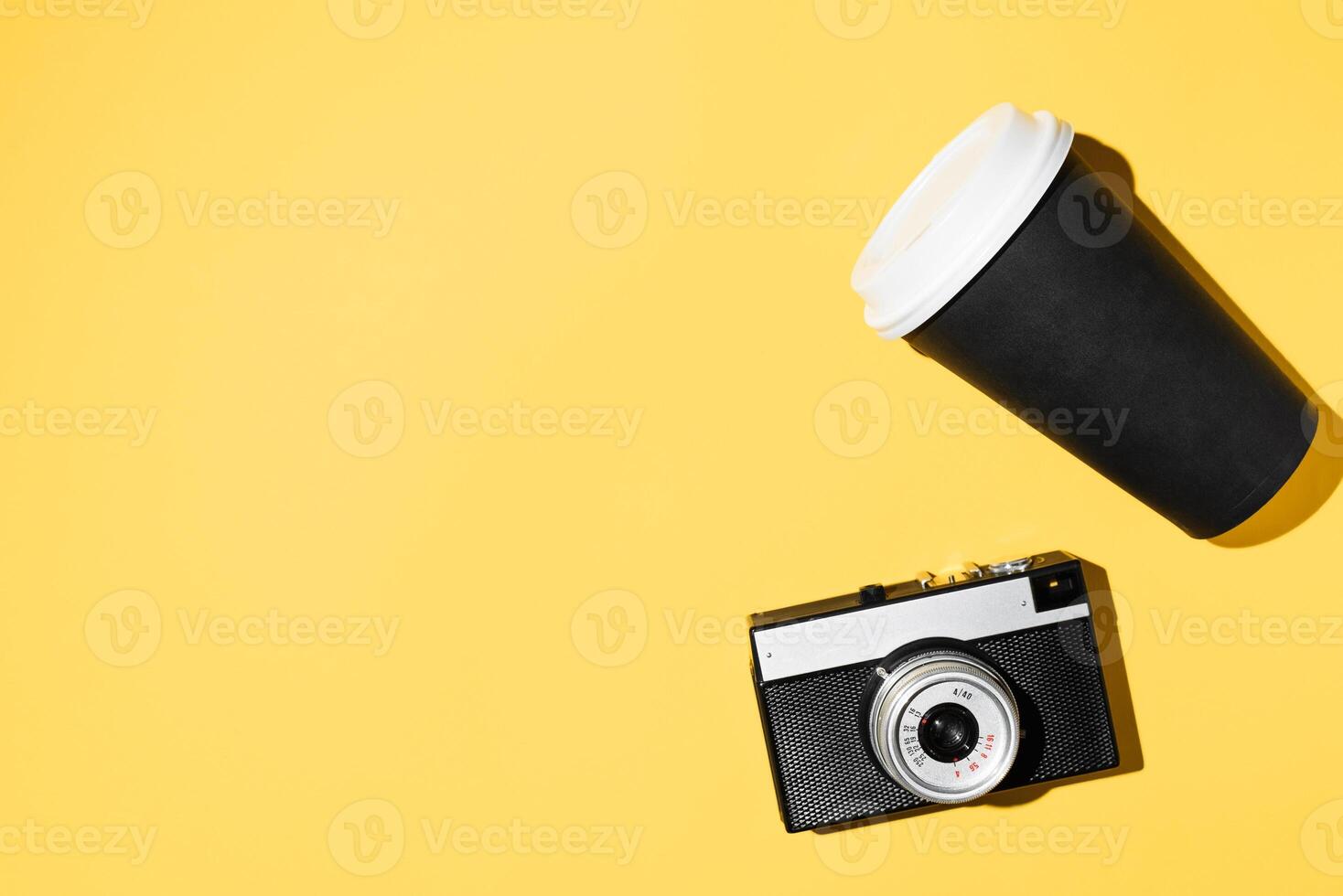 Vintage camera and disposable cup of coffee, flat lay. Yellow background, copy space. Hipster Walking Kit photo