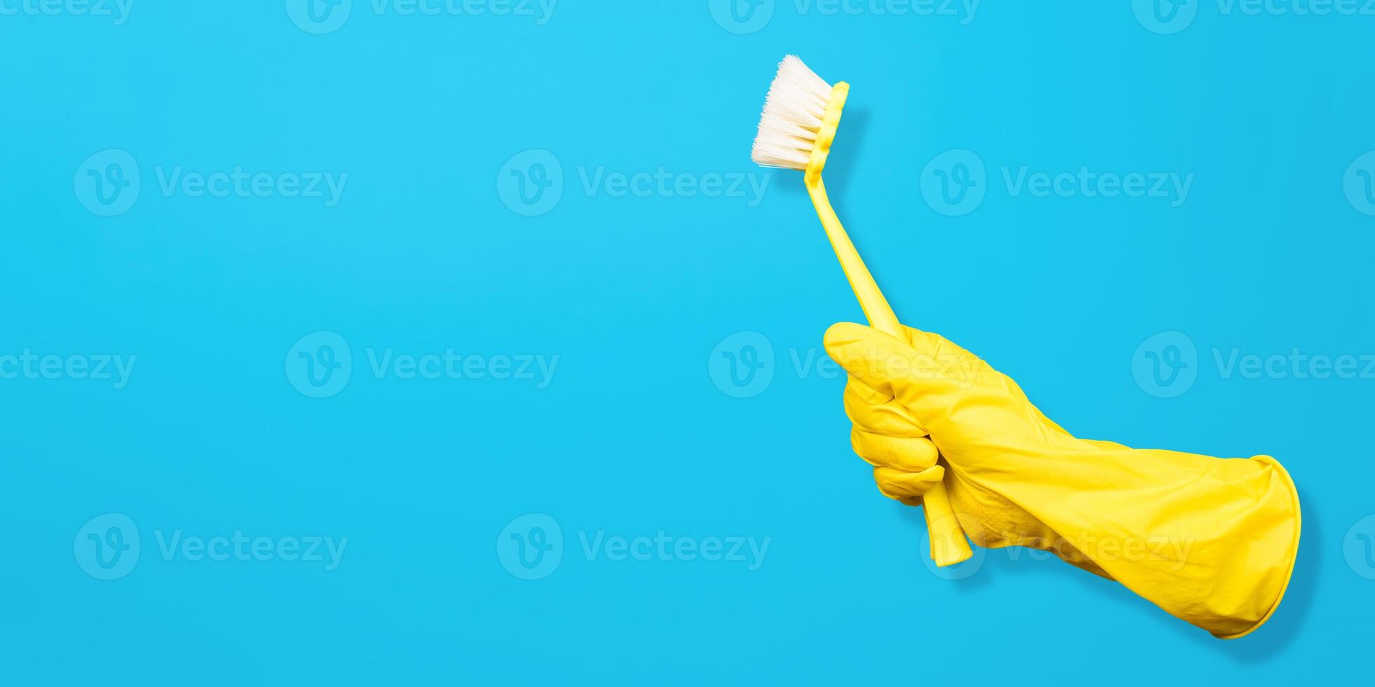 Invisible gloved hand holding cleaning brush. Blue background, copy space. Levitating objects. Creative concept for cleaning and washing equipment. photo