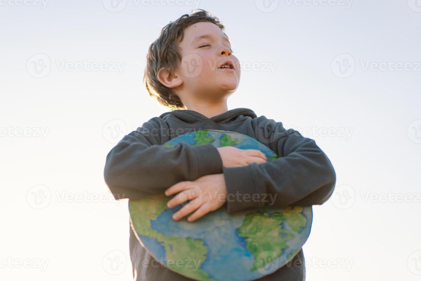 Little boy holding planet in hands against green spring background. Earth day photo