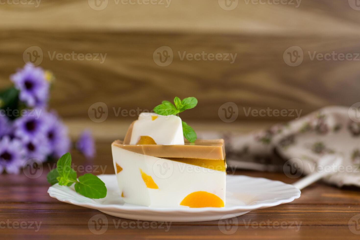 milk jelly dessert with pieces of fruit inside, in a plate on a wooden table photo