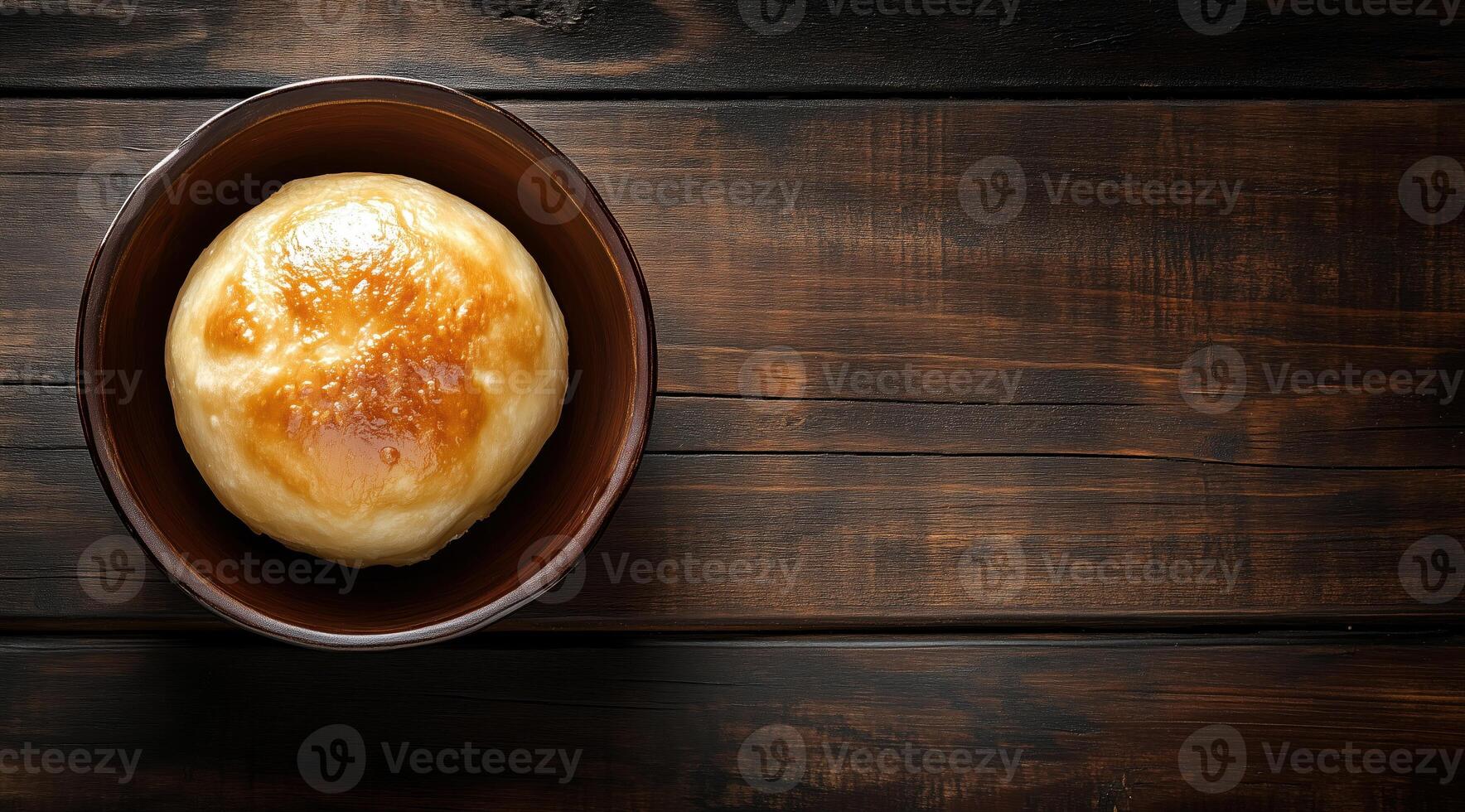 Golden baked bread roll on a rustic wooden table in dim light photo