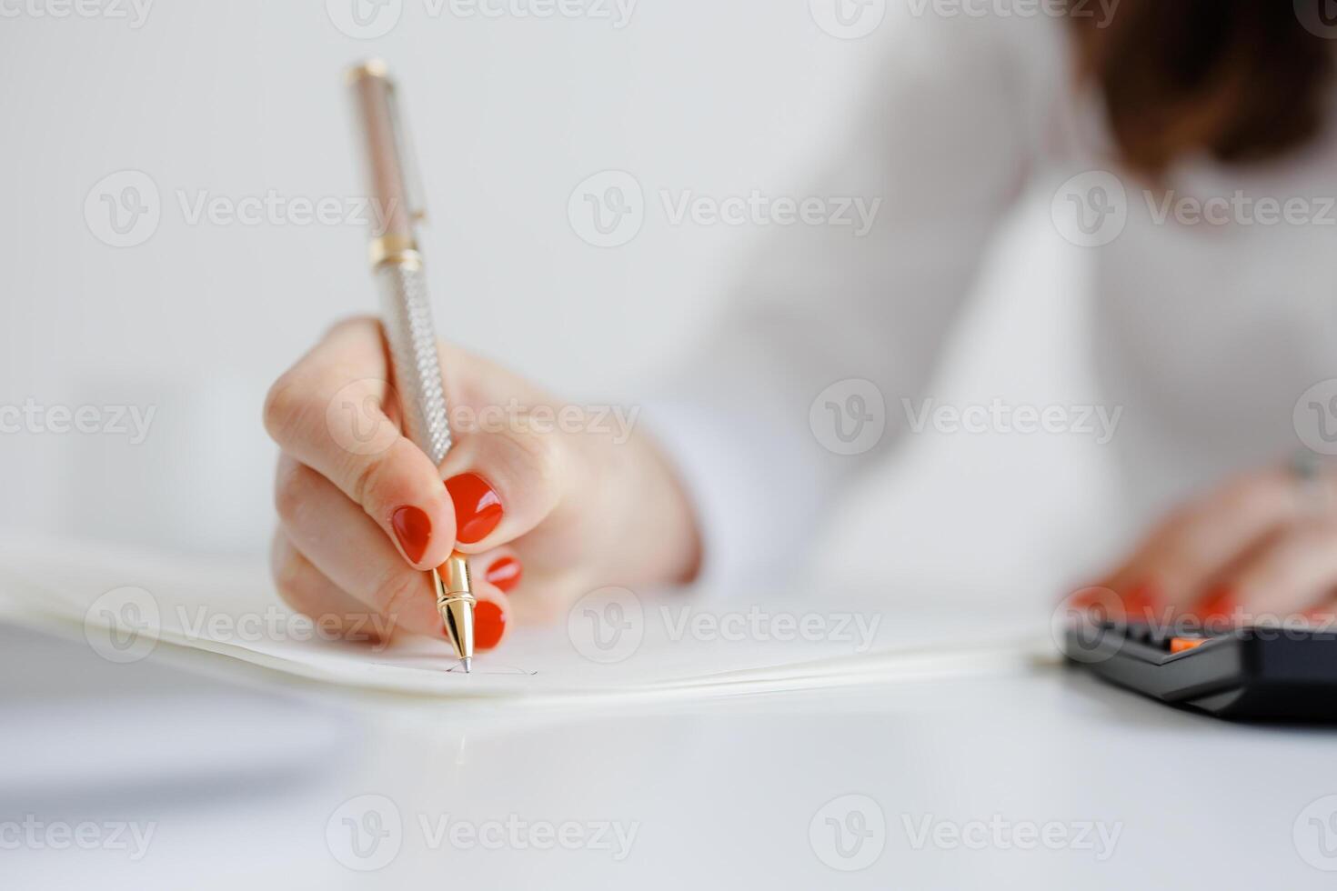 Woman writing notes with a pen and calculator on a desk during a work session in a bright, minimalist office space photo