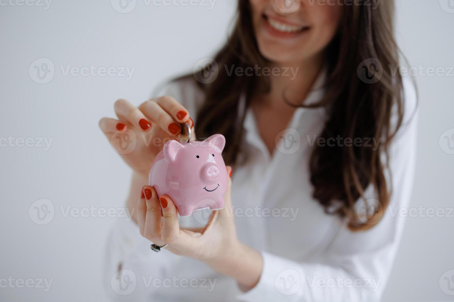 Woman saving money in a pink piggy bank at home while smiling during daytime photo