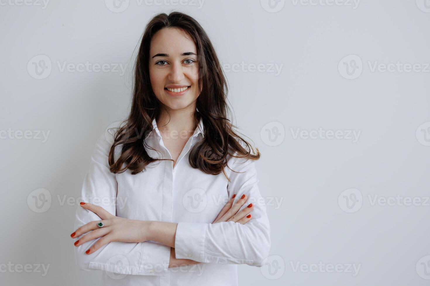 Young woman smiling confidently with arms crossed in front of a neutral background during a casual indoor setting photo