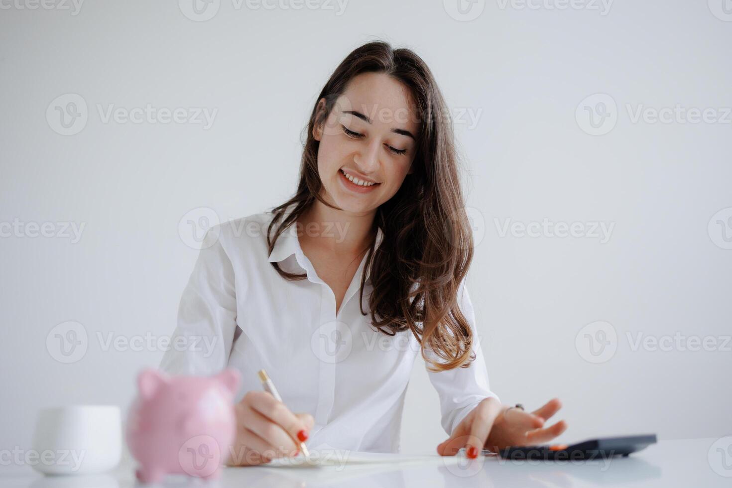 Woman writing notes at a desk with a piggy bank and calculator in a bright minimalist workspace photo