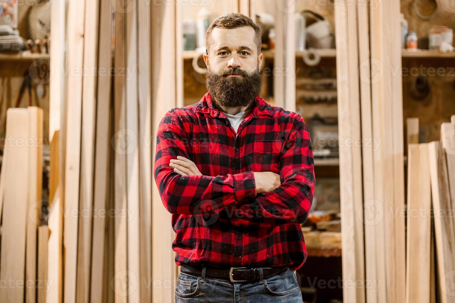 Craftsman stands confidently in woodworking shop surrounded by timber and tools in a cozy workshop environment photo