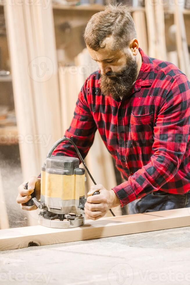 Skilled woodworker uses routing tool in workshop during daytime to shape wooden planks for custom furniture projects photo