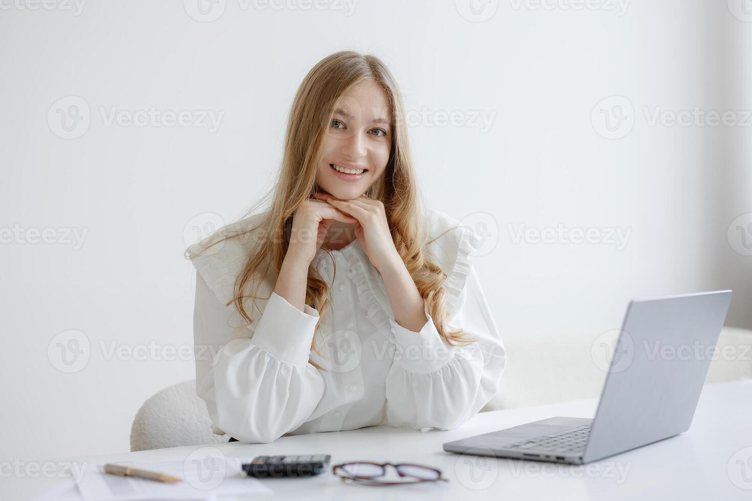 Young woman working at desk smiling with laptop during bright afternoon in minimalist workspace photo