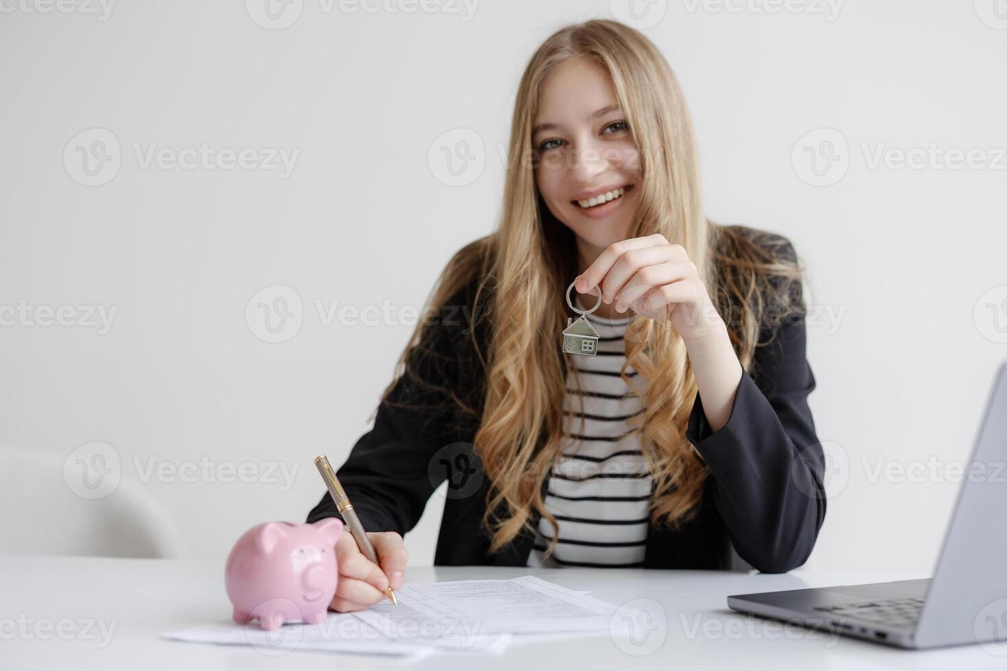 Real estate agent holding house key while finalizing paperwork with savings piggy bank on desk photo