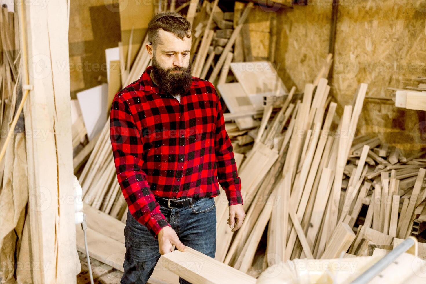 Craftsman in a woodworking shop selects timber while surrounded by raw materials, showcasing skill and creativity in a rustic setting photo