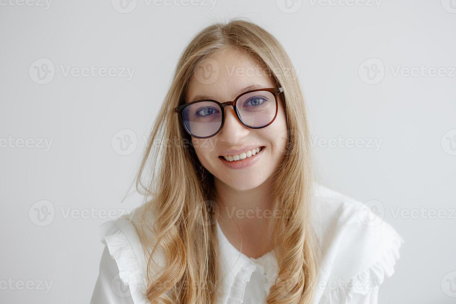 Young woman with glasses smiles warmly while sitting against a light background in a bright indoor space photo