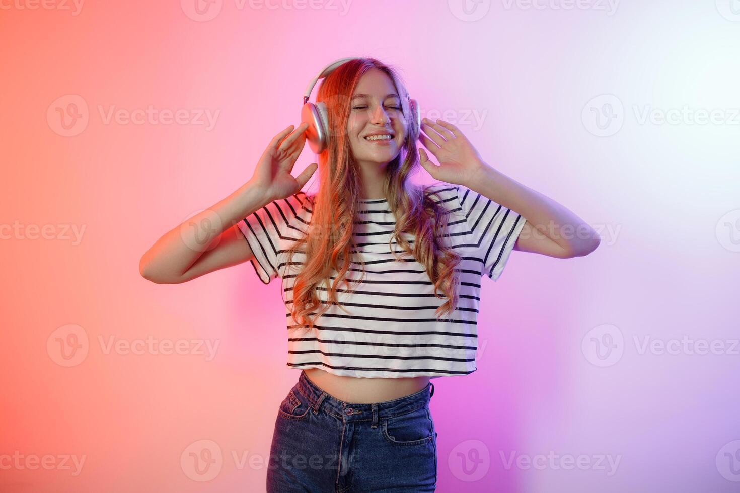 Young woman enjoying music with headphones while posing against a colorful background in a studio setting photo