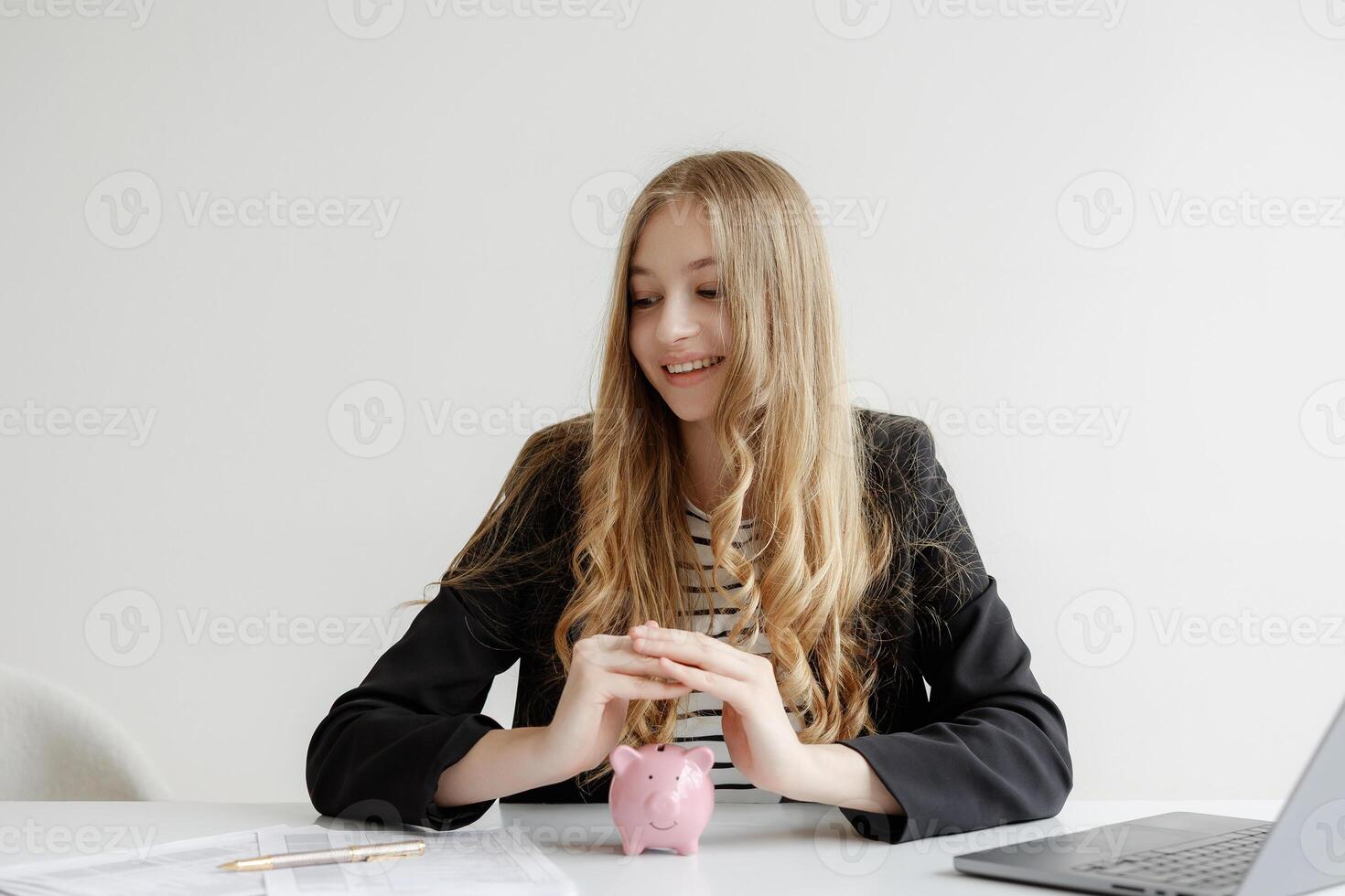 Young woman saving money with a piggy bank on a desk in a minimalist office setting during the day photo