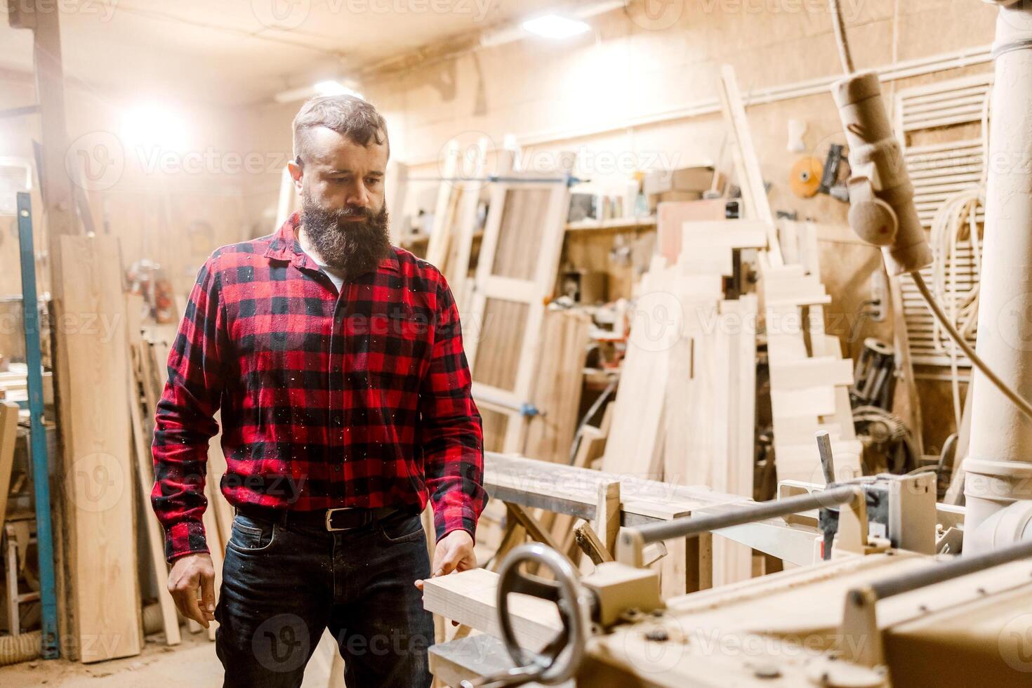 Skilled carpenter working in a workshop surrounded by wood and tools during the day photo