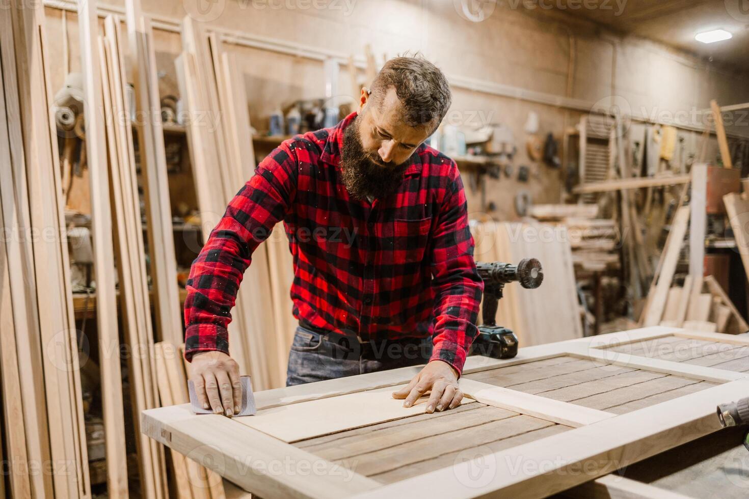 Skilled carpenter works on crafting a wooden door in a workshop during daylight hours photo