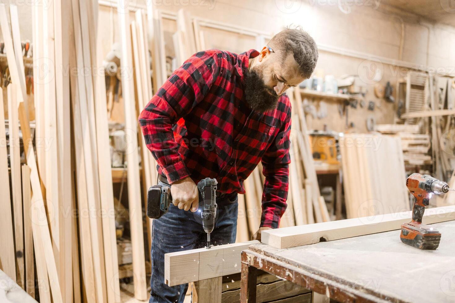 Craftsman using a power drill to work on wooden boards in a workshop during the day photo