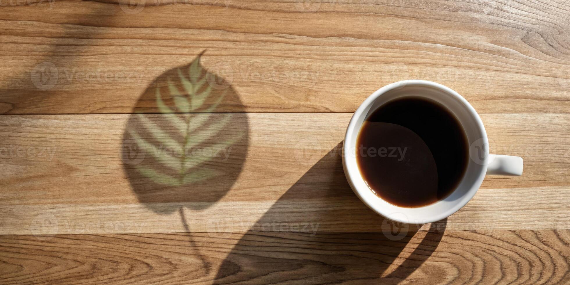 Coffee cup casting a leaf shadow on wooden table. photo