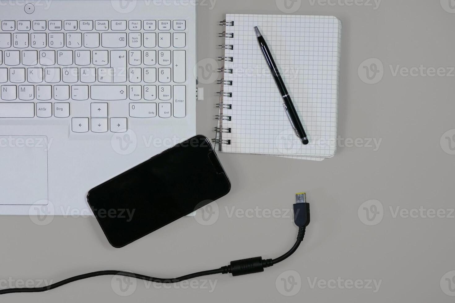 Flat lay on white background top view with copy space. Computer laptop keyboard, notebook, smartphone and cable. The concept of business, study or IT photo