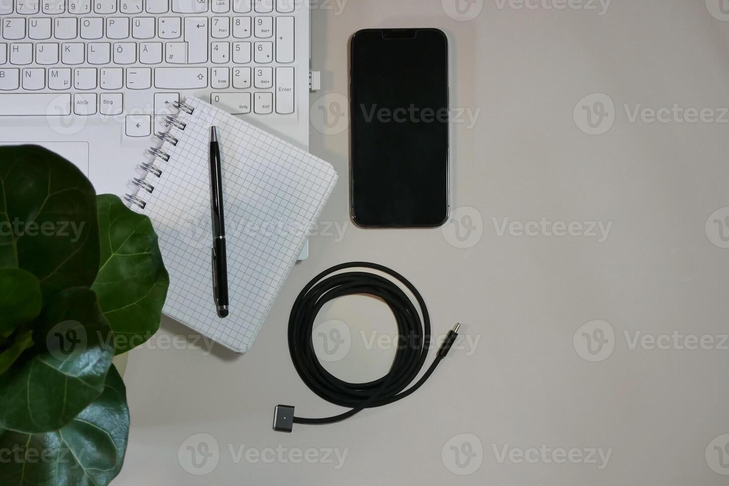Flat lay on white background top view with copy space. Computer laptop keyboard, notebook, smartphone, house plant and cable. The concept of business, study or IT photo